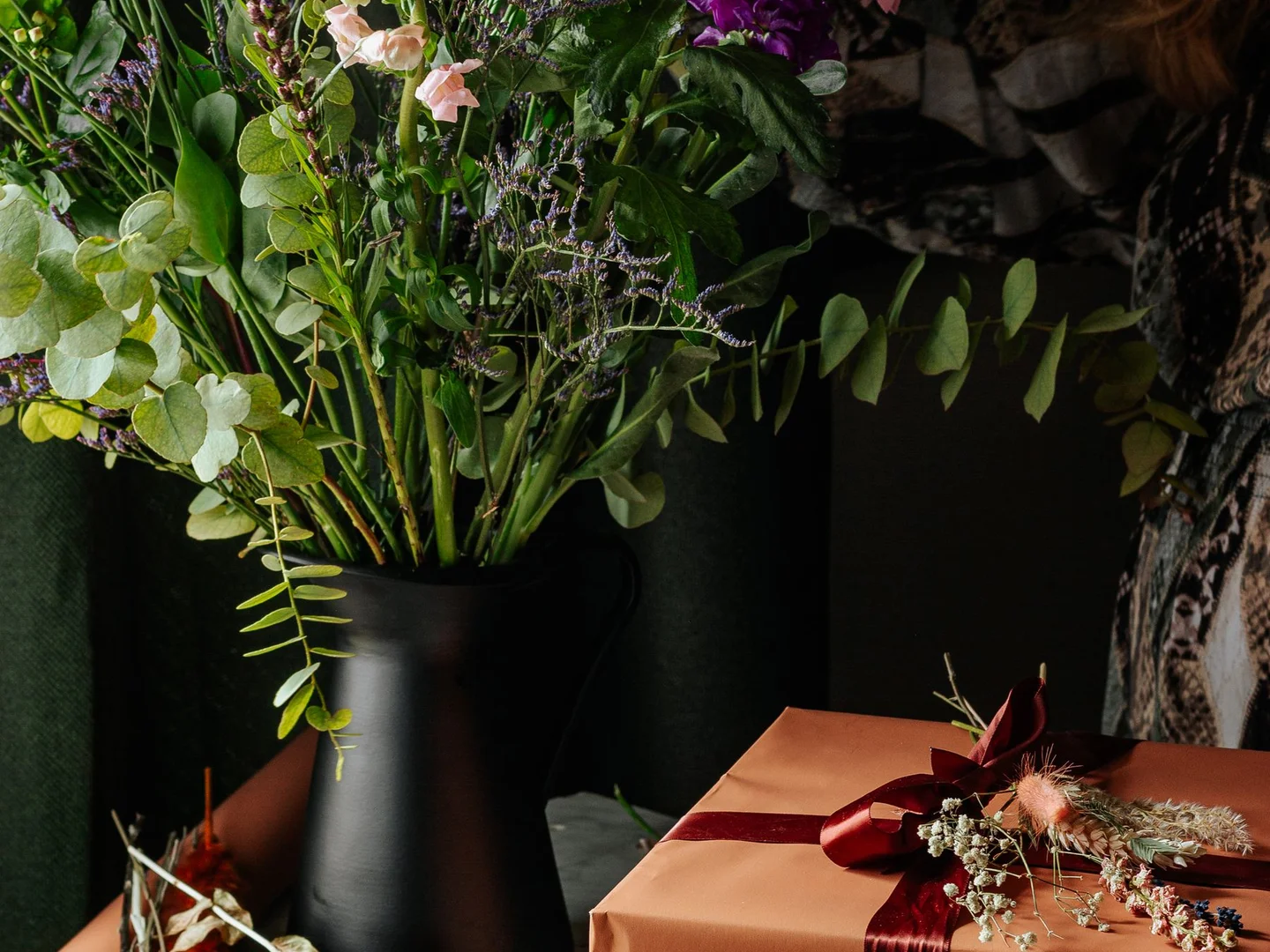 A flower arrangement in a vase beside a wrapped gift.