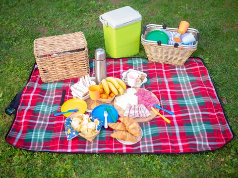 A picnic blanket with reusable cups, plates and food containers.