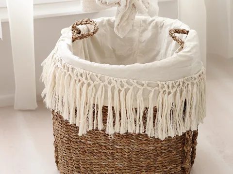 A hand placing laundry into a woven hamper.