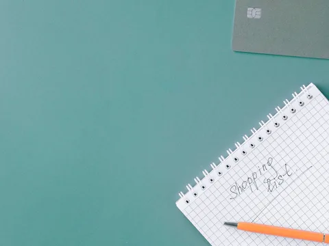A spiral notebook with a shopping-list heading and pencil.