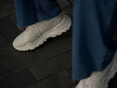 White low-top sneakers worn with blue denim jeans.
